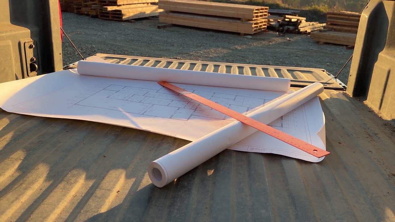 Site drawings and a folding rule open on a pickup tailgate at a lumber yard